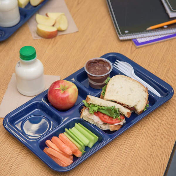 A Carlisle dark blue school lunch tray with a sandwich, carrots, and apples.