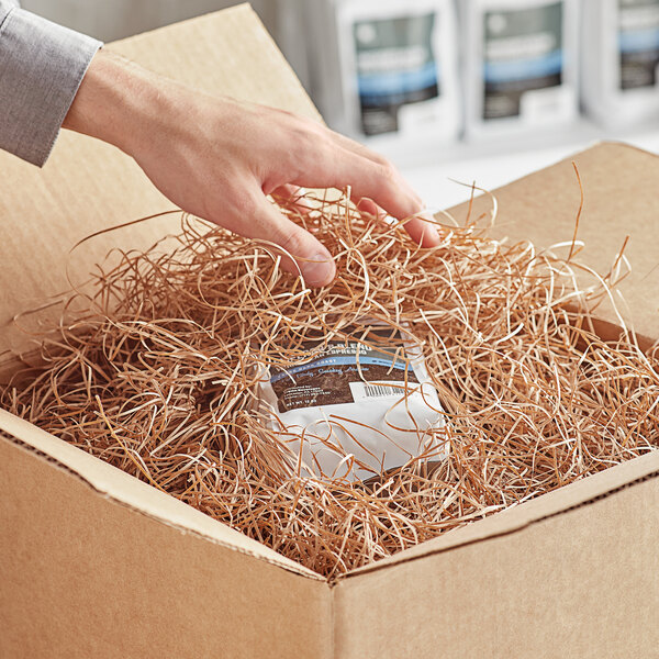 A hand reaching out to a package in a cardboard box with Kraft paper shred inside.