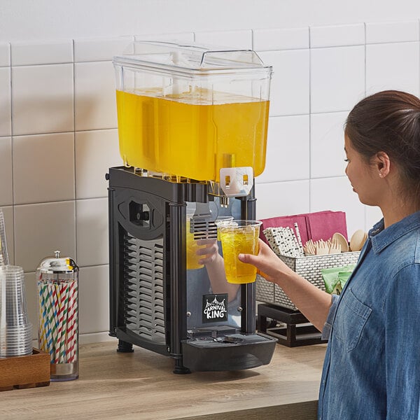 A woman pouring orange juice into a Carnival King refrigerated beverage dispenser.