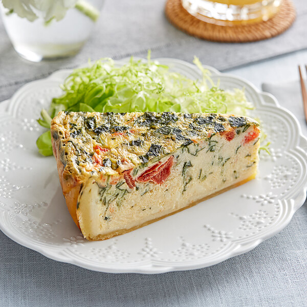 A slice of Priscilla's 5-Slice Spinach and Tomato Quiche with vegetables on a plate.