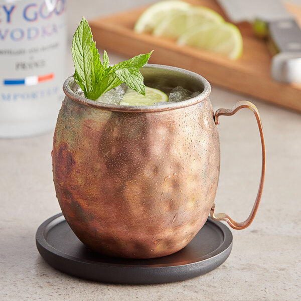 An Acopa Alchemy hammered dark antique copper Moscow Mule mug with a drink, lime, and mint leaves.