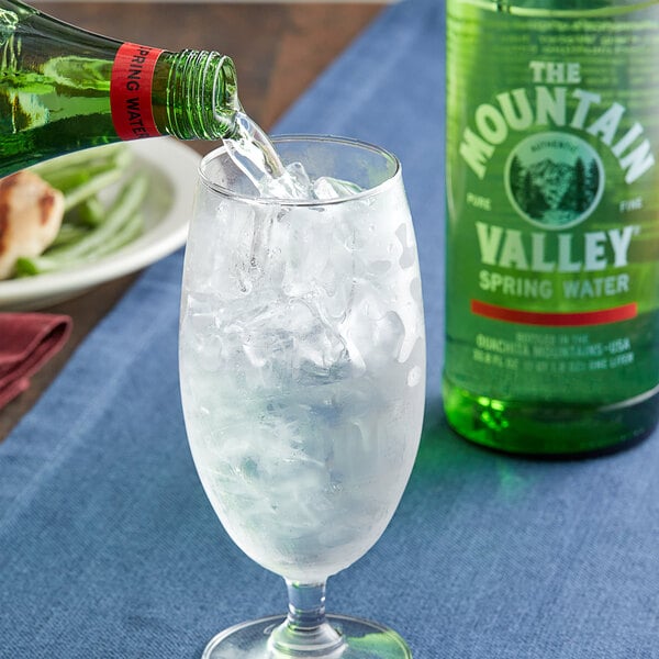 A close up of a green Mountain Valley Spring Water glass bottle being poured into a glass with ice.