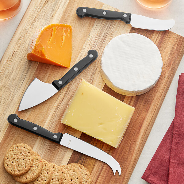 Acopa cheese knives next to cheese and crackers on a wooden cutting board.
