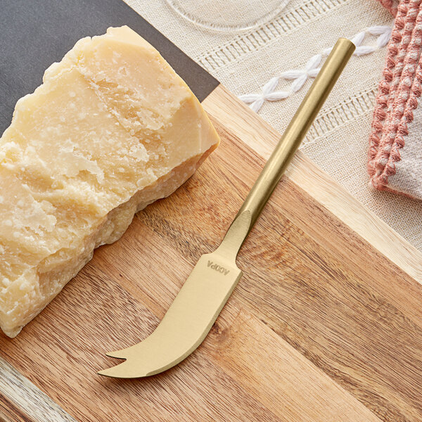 An Acopa gold stainless steel cheese knife with a piece of cheese on a cutting board.