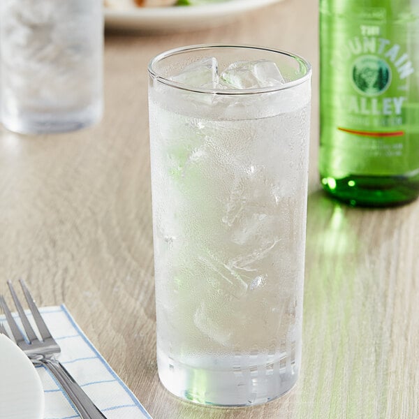 A glass of Mountain Valley Spring Water with ice and a bottle of beer on a table.