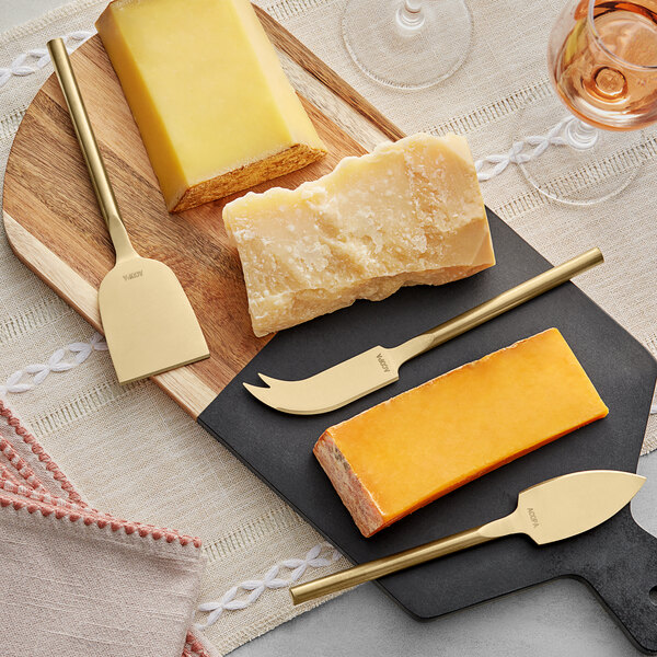 A block of cheese on a cutting board with Acopa gold cheese knives and glasses of wine.