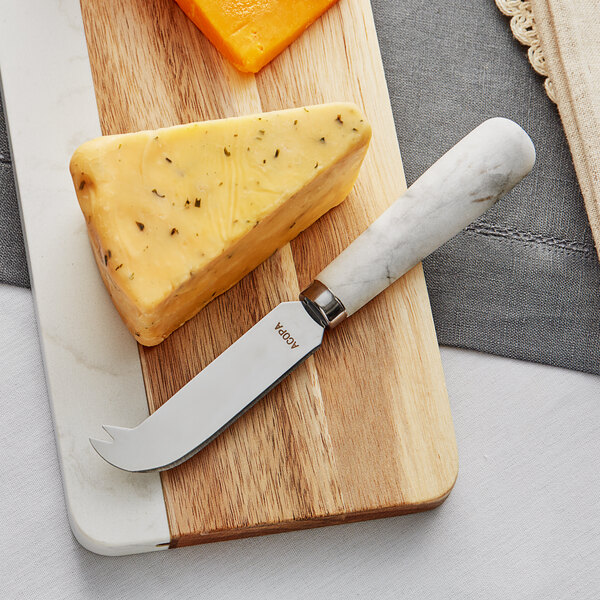 An Acopa cheese knife on a cutting board with cheese.