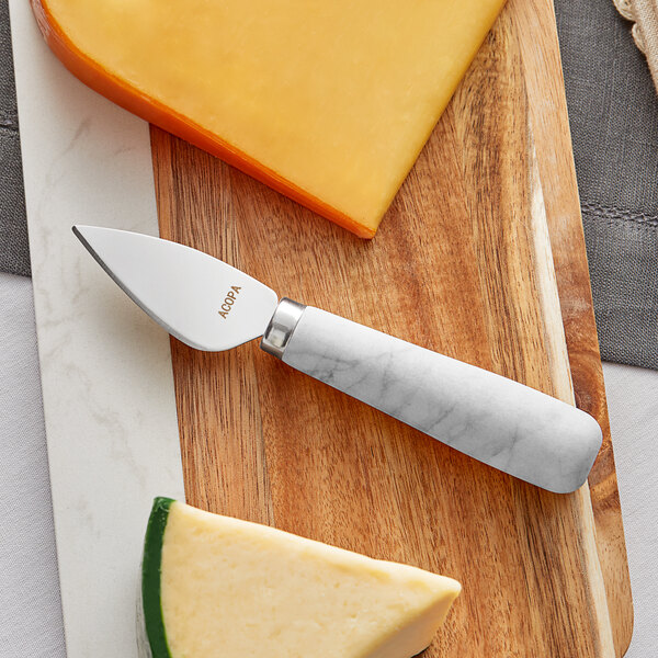 An Acopa stainless steel cheese knife with a white marble handle cutting cheese.