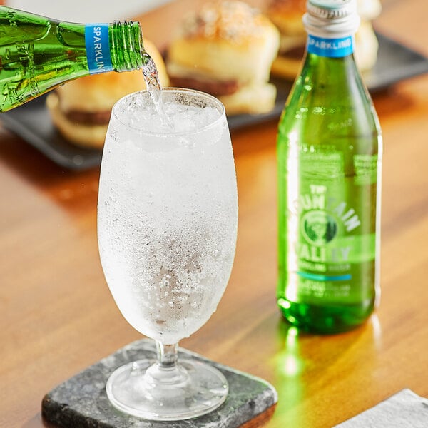 A person pouring Mountain Valley Sparkling Water from a green glass bottle into a glass.