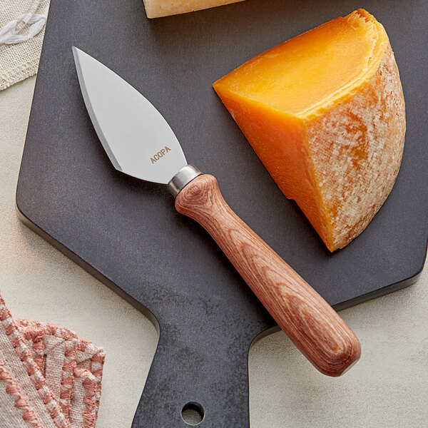 An Acopa cheese knife cutting a block of cheese on a cutting board.