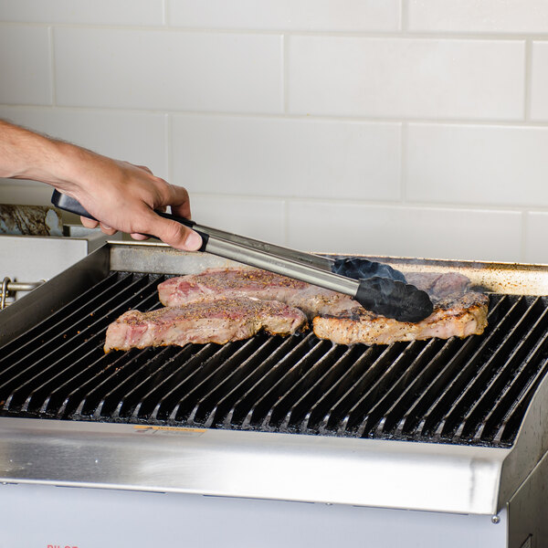 A person using Vollrath Jacob's Pride tongs to cook meat on a grill.