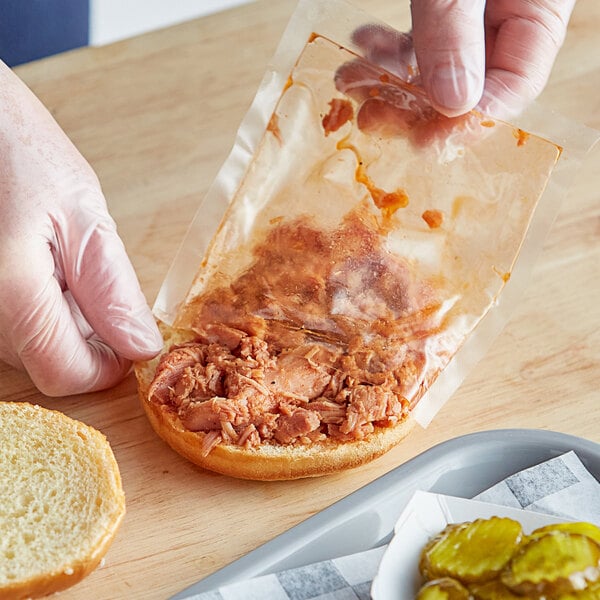 A person holding a sandwich with Riffs Smokehouse pulled chicken on a counter in a deli.