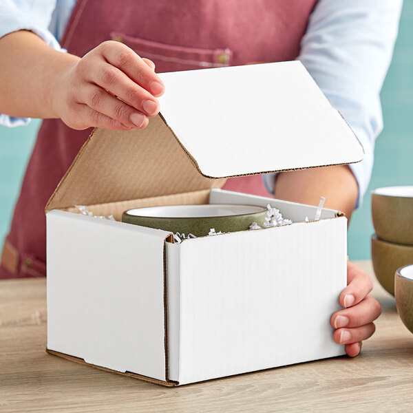 A person opening a white Lavex corrugated mailer box to reveal a bowl inside.