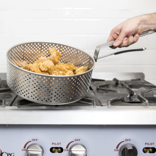 A person using a Vollrath replacement basket to fry chicken in a fryer pot on a stove.