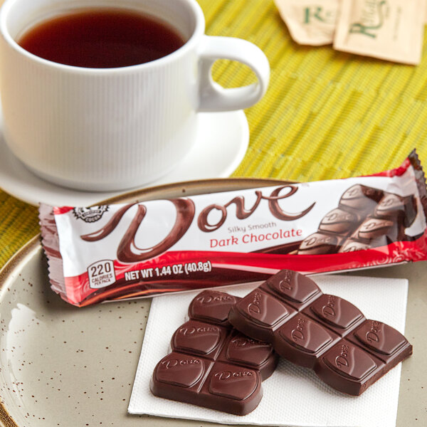 A DOVE dark chocolate bar with a logo on the wrapper on a table near a cup of tea.