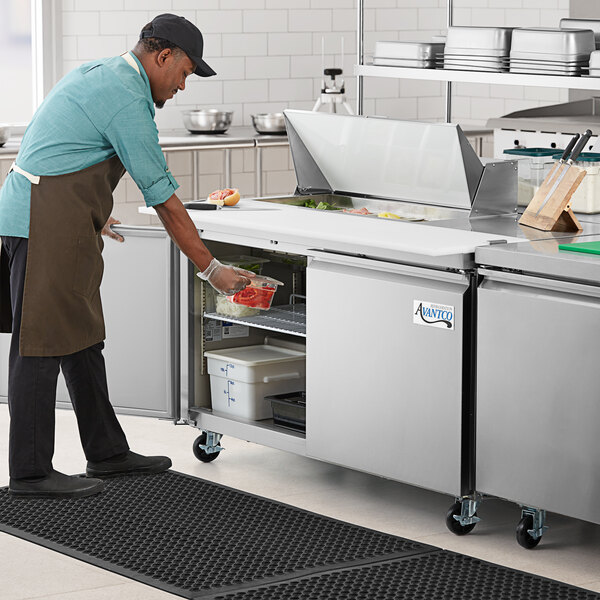 An Avantco stainless steel refrigerator with a man putting food inside.
