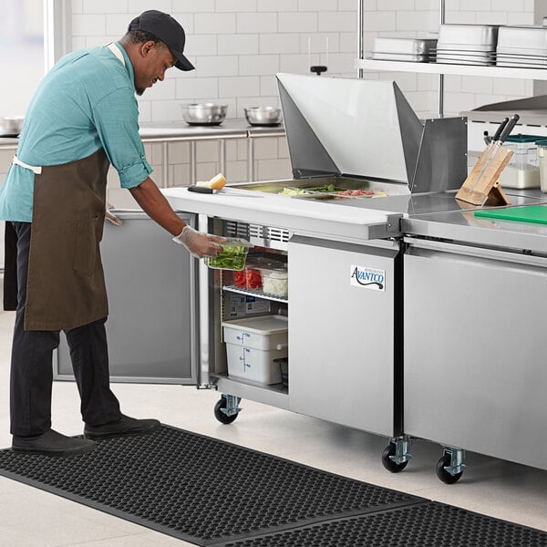 An aproned man in a professional kitchen using an Avantco stainless steel sandwich prep table.