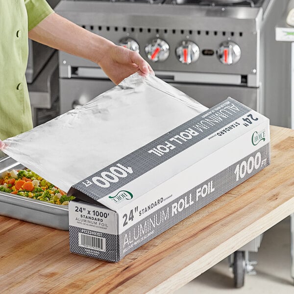 A woman using Choice Food Service Standard Aluminum Foil to cover a tray of food on a counter.