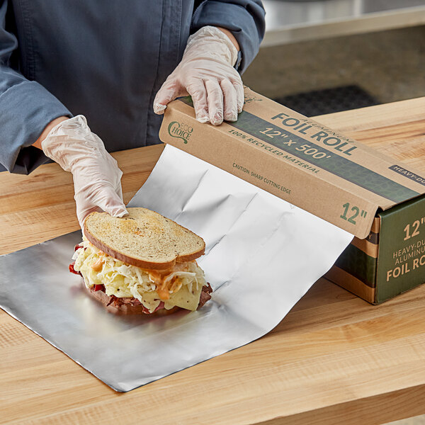 A person in white gloves using EcoChoice aluminum foil to wrap a sandwich.