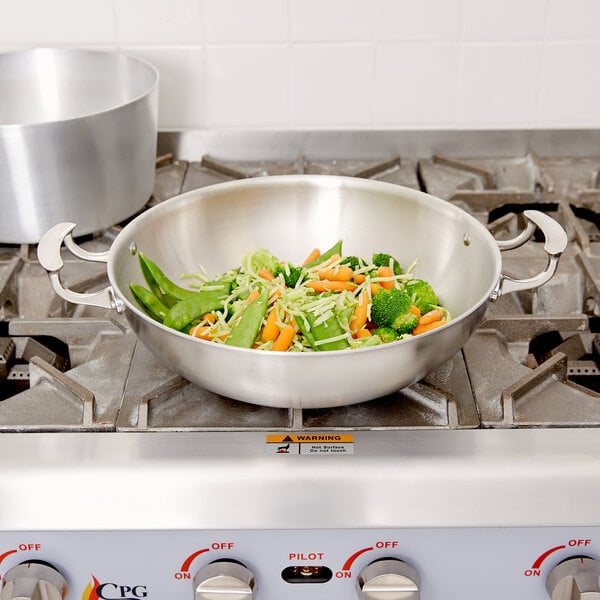 A Vollrath Miramar stir fry server with vegetables in a pan on a stove.