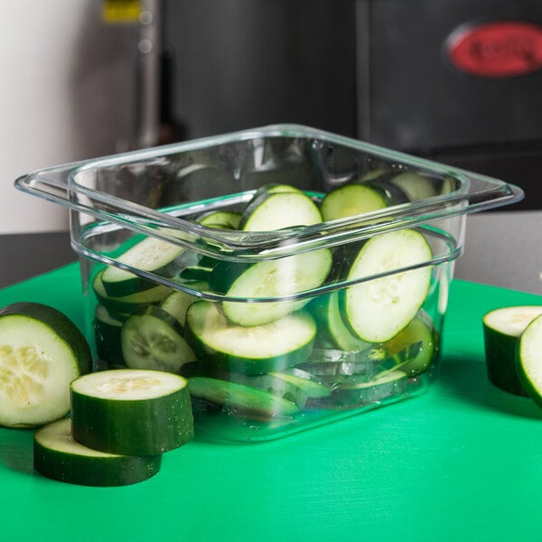 A Cambro clear plastic food pan holding cucumber slices on a green surface.