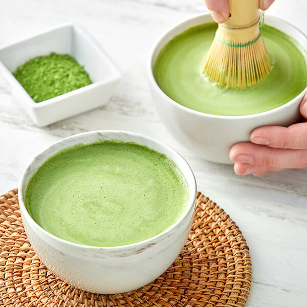 A person mixing Jade Leaf matcha in a white bowl with a bamboo whisk.