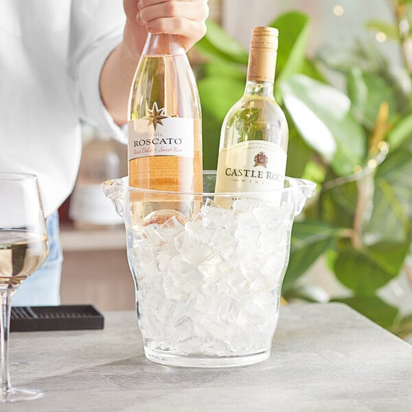 A person holding a bottle of wine in a Choice clear plastic wine bucket filled with ice on a table.