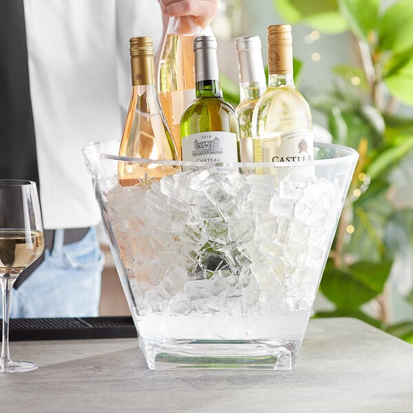A man pouring wine into a clear plastic wine bucket filled with ice on a table.