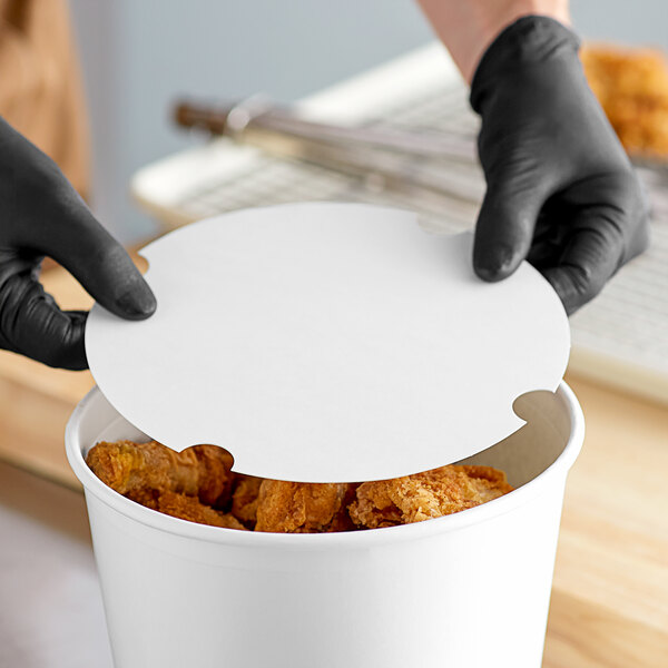 A person wearing black gloves places a white Innopak paper lid on a container of fried chicken.