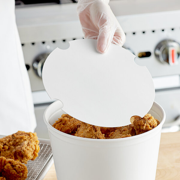 A gloved hand placing a white Innopak paper lid on a bucket of fried chicken.