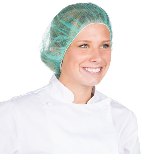 A woman wearing a white chef's coat and a green Royal Paper bouffant cap.