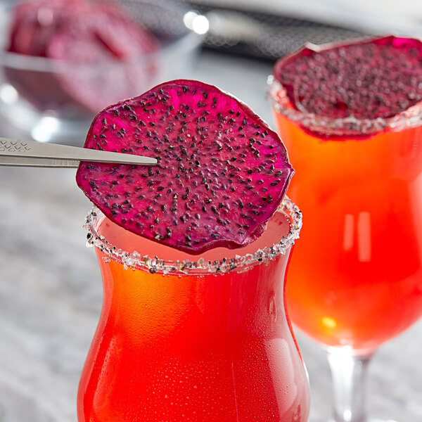 Two glasses of red and purple drinks with red dragon fruit slices on top.