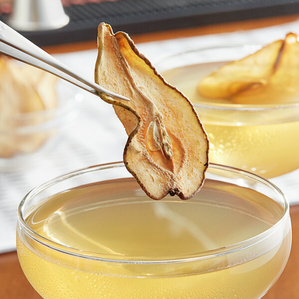 Dried pear slices on tongs above a glass of liquid.