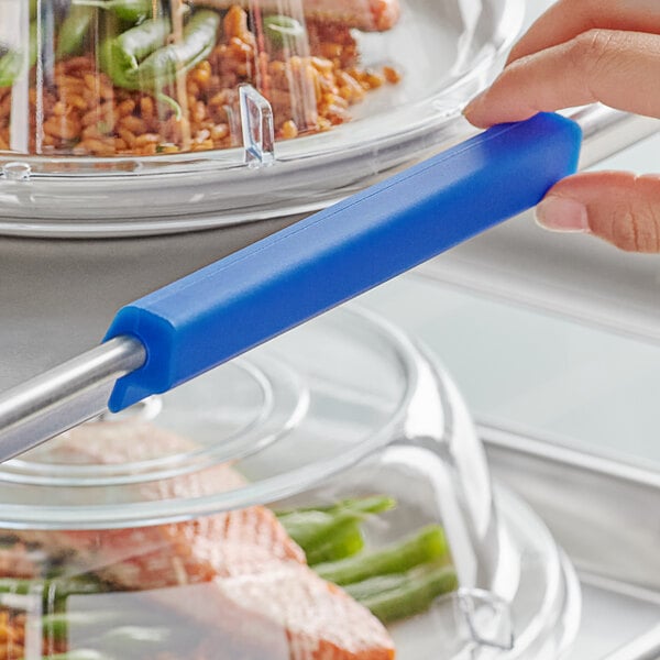 A person using a Baker's Mark blue silicone sheet pan clip to identify a glass container of food.
