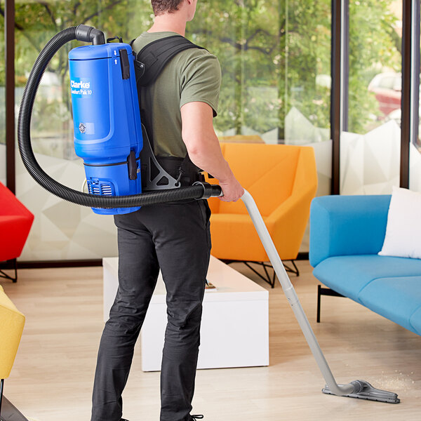 A man using a Clarke Comfort Pak backpack vacuum to clean a room.