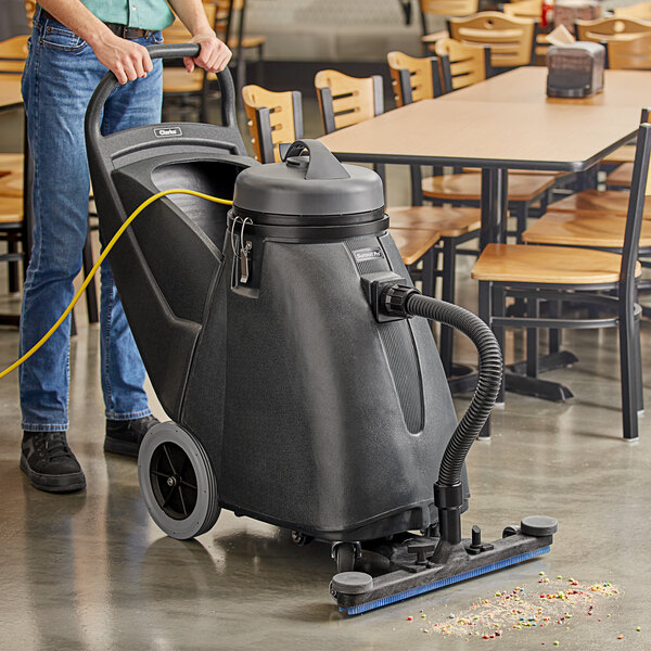 A man using a Clarke Summit Pro wet/dry vacuum with a squeegee attachment to clean a floor in a restaurant.