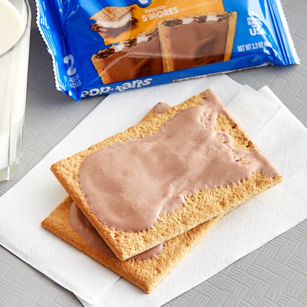 A close up of a box of Pop-Tarts Frosted S'mores Snack Bars with two pastries on a napkin.