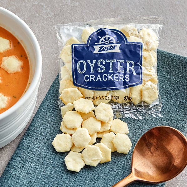 A bowl of soup with a bag of Zesta oyster crackers and a spoon.