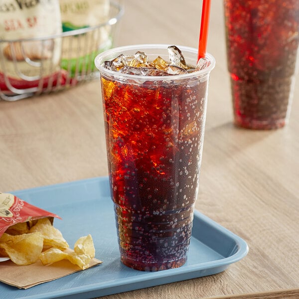 A clear plastic cup filled with soda and ice on a tray with chips.