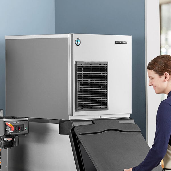 A woman in a corporate office cafeteria standing next to a Hoshizaki air cooled flake ice machine.
