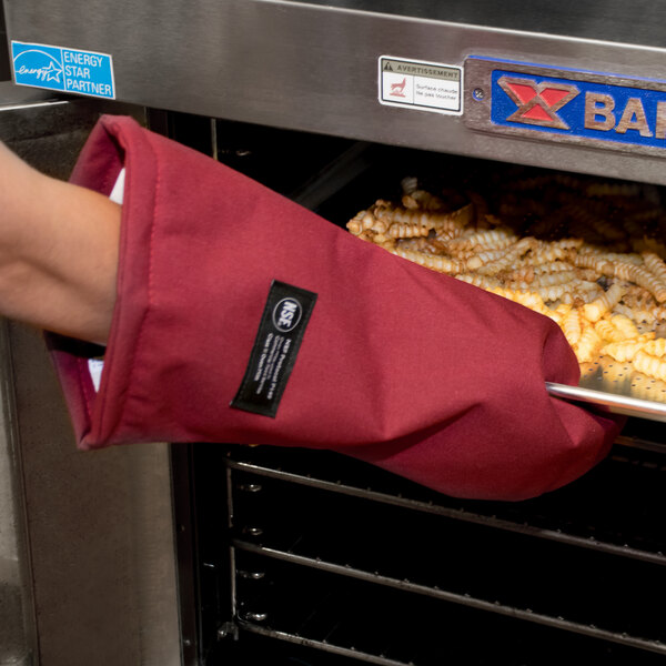 A person wearing a San Jamar Cool Touch Flame oven mitt holding a metal tray of food.