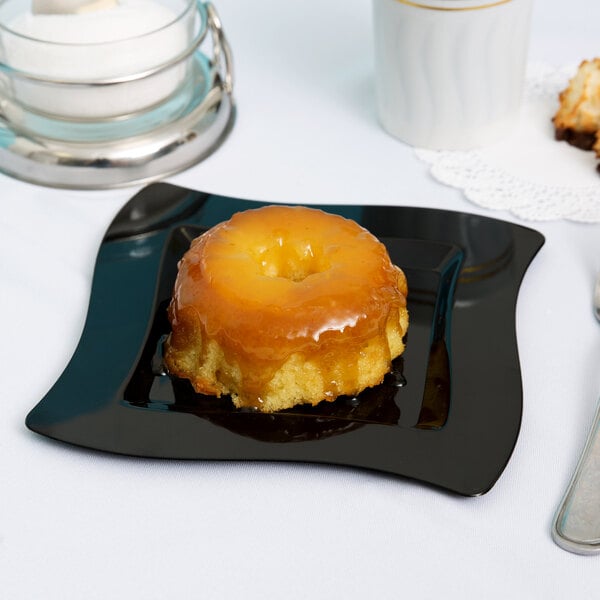 A Fineline black plastic square plate with a small cake on it.