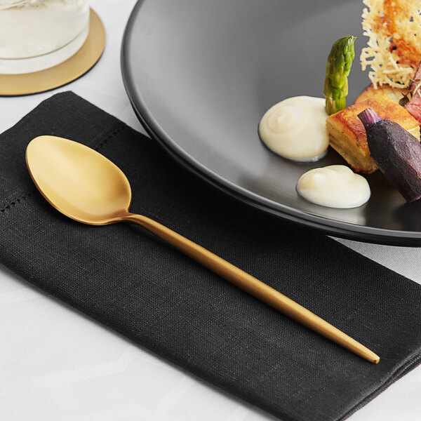 A plate of food on a black napkin with an Acopa Odin brushed stainless steel dinner spoon.