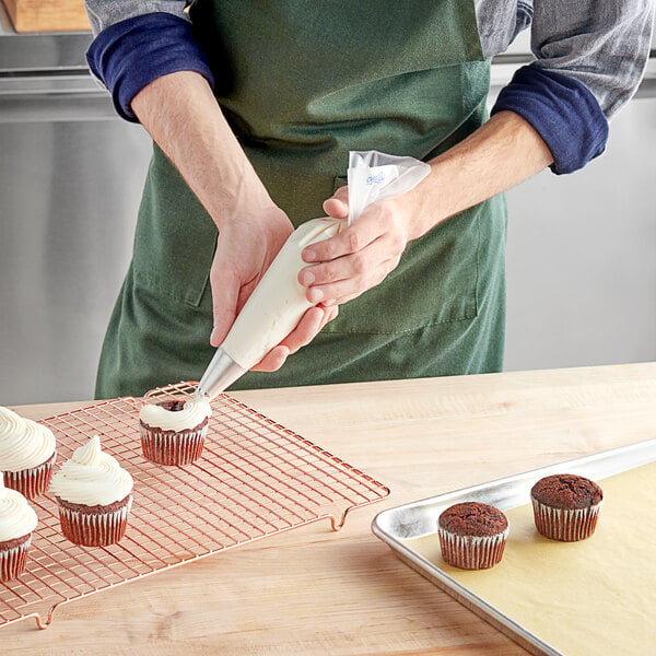 A person in a professional kitchen using an Enjay disposable pastry bag to frost a cupcake.