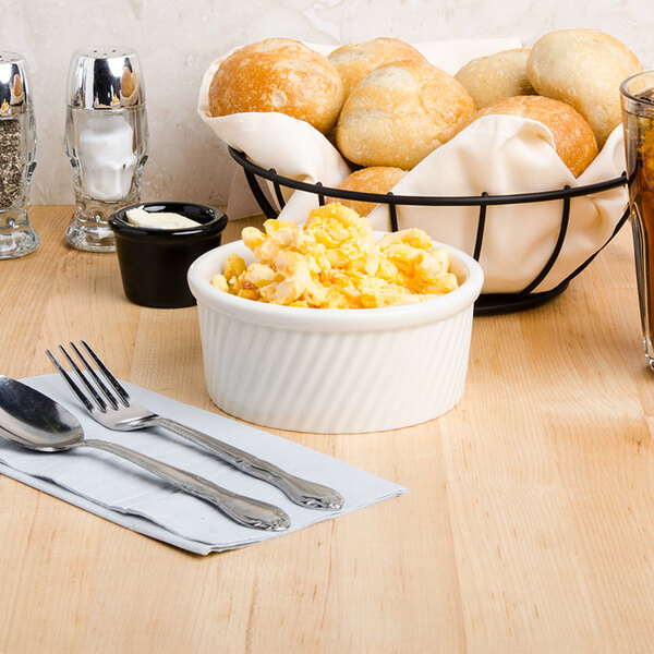 A Tuxton eggshell swirl ramekin filled with food on a table with a basket of bread and a glass of beer.