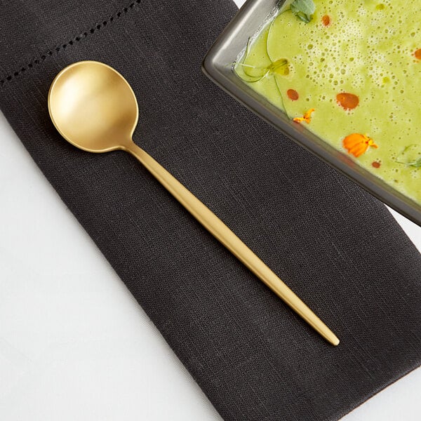 An Acopa Odin brushed stainless steel bouillon spoon in a bowl of green soup.