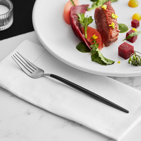 A plate with a fork and knife on it next to a plate of food with an Acopa Odin brushed stainless steel dinner fork on it.
