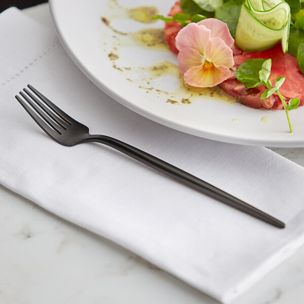 An Acopa Odin stainless steel salad fork on a white plate with food.