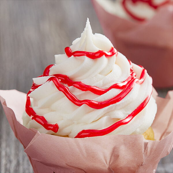 A cupcake with white frosting and red drizzle.