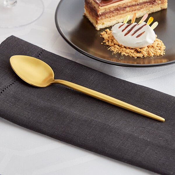 An Acopa Odin gold stainless steel teaspoon on a plate with a dessert.
